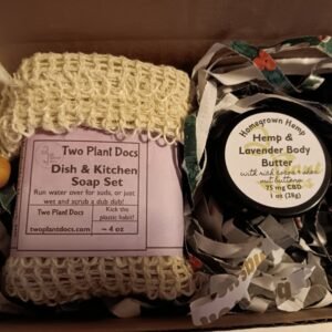 An open gift box containing a soap inside a sisal scrubbie/soap saver and a jar of body butter